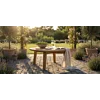 Luxe ronde teakhouten loungetafel in een zonnige tuinsetting met lavendel, rozen en een linnen plaid op een stenen terras.