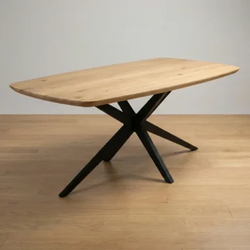 Vrijstaande eiken eettafel met Deens ovaal blad en zwarte stalen spinpoot tegen een neutrale achtergrond.