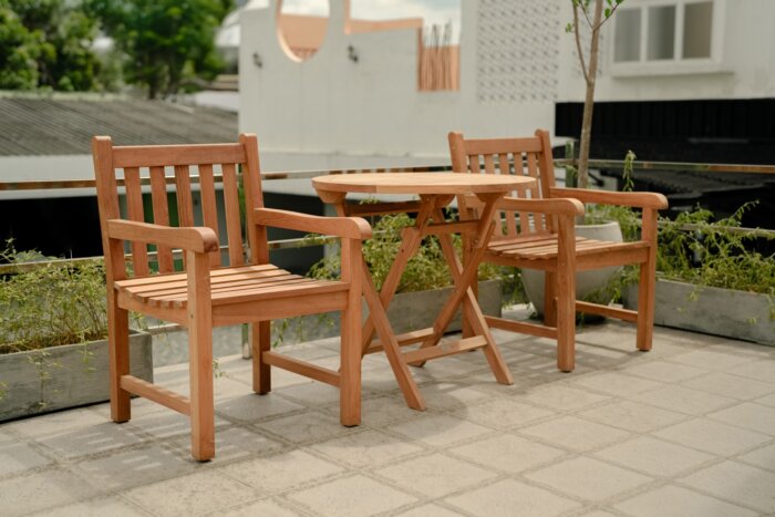 Teakhouten tuinset bestaande uit twee klassieke Windsor stoelen en een ronde, inklapbare tuintafel (Ø 80cm), opgesteld in een sfeervolle tuin.