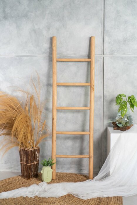 Natuurlijke teakhouten decoratieladder, met een hoogte van 175 cm, een breedte van 50 cm en een diepte van 5 cm. De ladder heeft diverse horizontale sporten, gelijkmatig verdeeld over de lengte, en staat licht hellend voor extra stabiliteit. Het onbehande