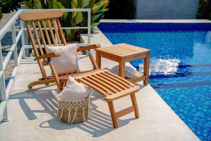 Luxe teakhouten deckchair met verstelbare rugleuning en voetensteun, geplaatst op een zonnig terras naast een zwembad.