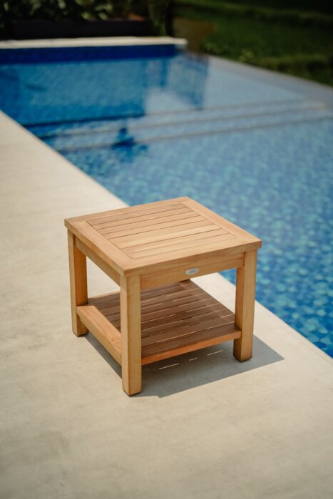 Stevige teakhouten tuin salontafel, afmetingen 50 cm lengte, 50 cm breedte en 45 cm hoogte, voorzien van een handig onderblad. De tafel heeft een natuurlijke teakkleur met een zichtbare houtnerf, wat bijdraagt aan een rustieke en natuurlijke uitstraling. 